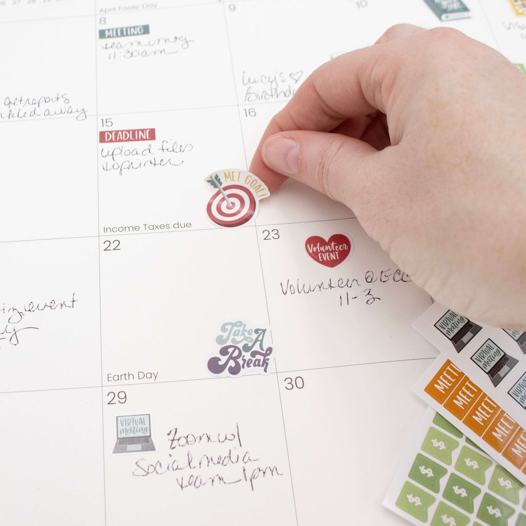 Person placing Bloom Workday Essentials Planner Sticker on a calendar, highlighting deadlines and events.