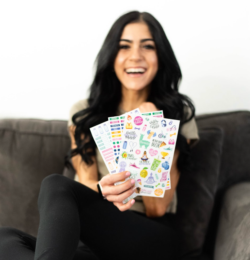 Woman holding up a pack of fanned out fitness themed stickers.