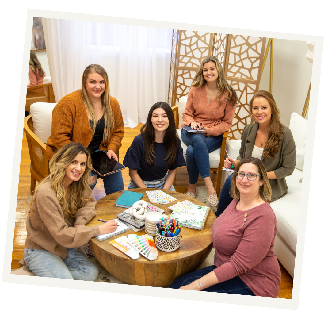six bloom daily planners team members sitting around a table with their bloom planner products smiling at the camera