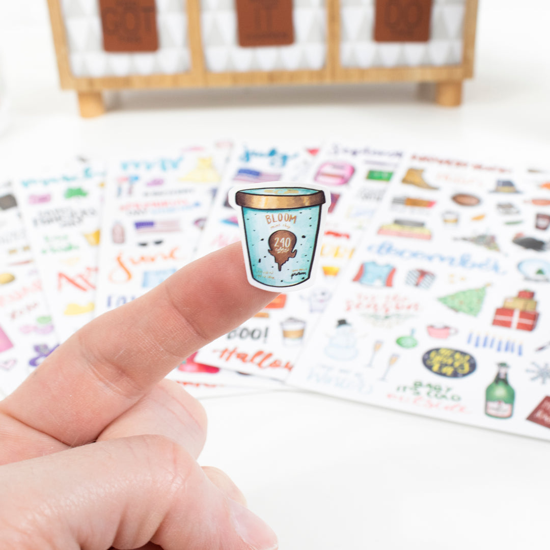 Hand holding a vintage holiday planner sticker on a finger, showcasing seasonal hand-drawn designs.
