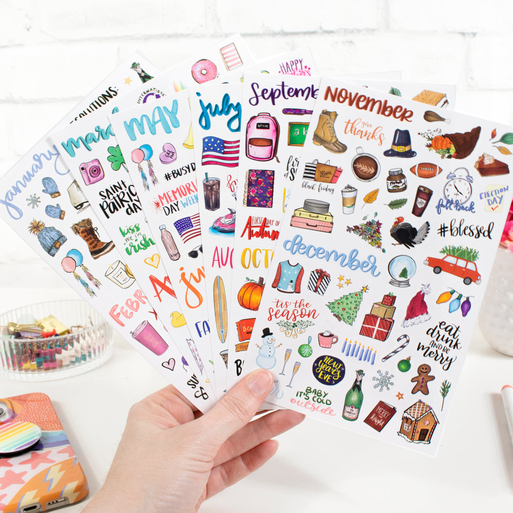 Hand holding seasonal planner stickers featuring vintage holiday designs, including months and festive illustrations.