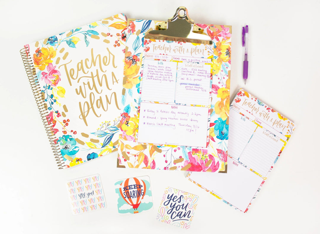A floral teacher planner, a floral clipboard, and a filled out daily teacher planning pad on a white desk with inspirational cards scattered around the desk.