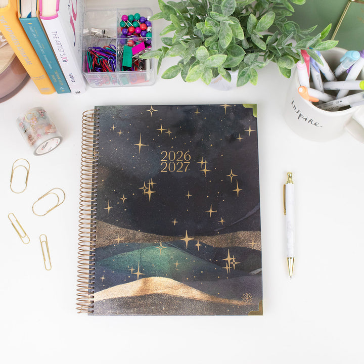 Spiral-bound planner with starry night design on a desk with stationery items