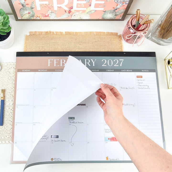 Hand tearing a January 2027 page off a desk calendar to reveal the February 2027 page.