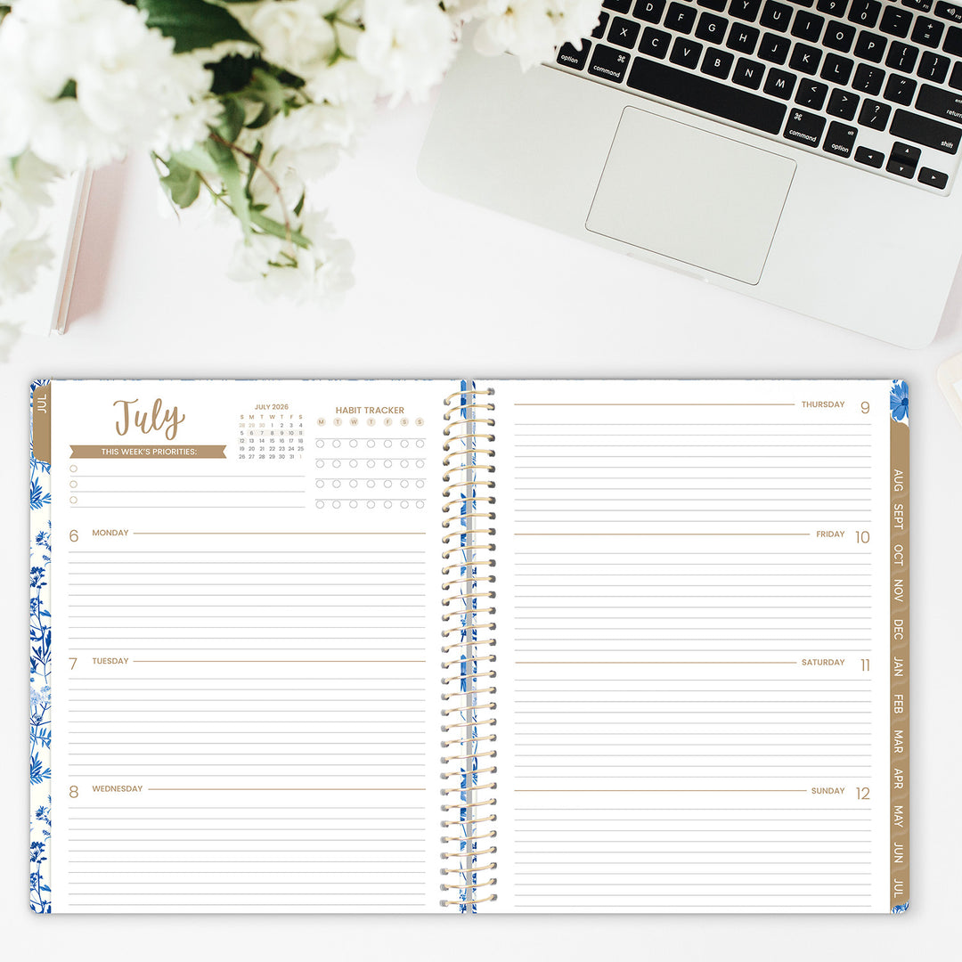 Open planner with floral design on a desk with a laptop and flowers.
