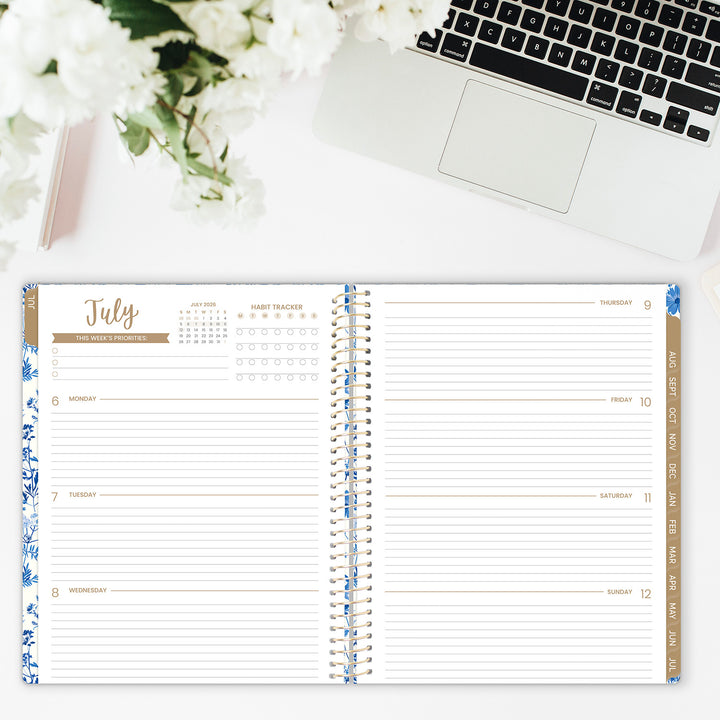 Open planner with floral design on a desk with a laptop and flowers.