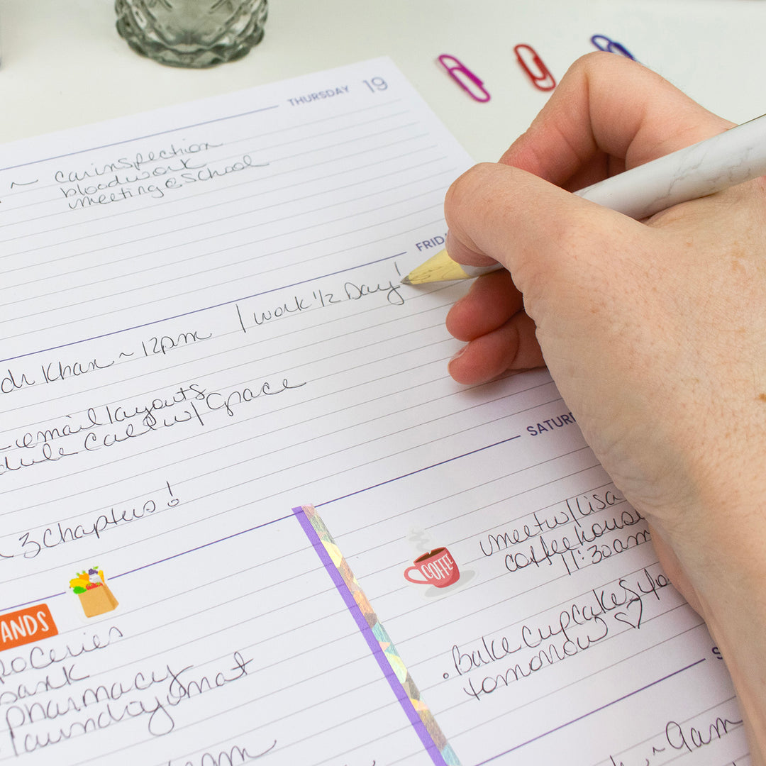 Someone writing in a weekly view of a planner.