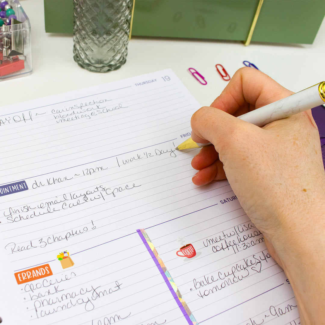 Hand holding a pen over a planner with notes and colorful stickers.
