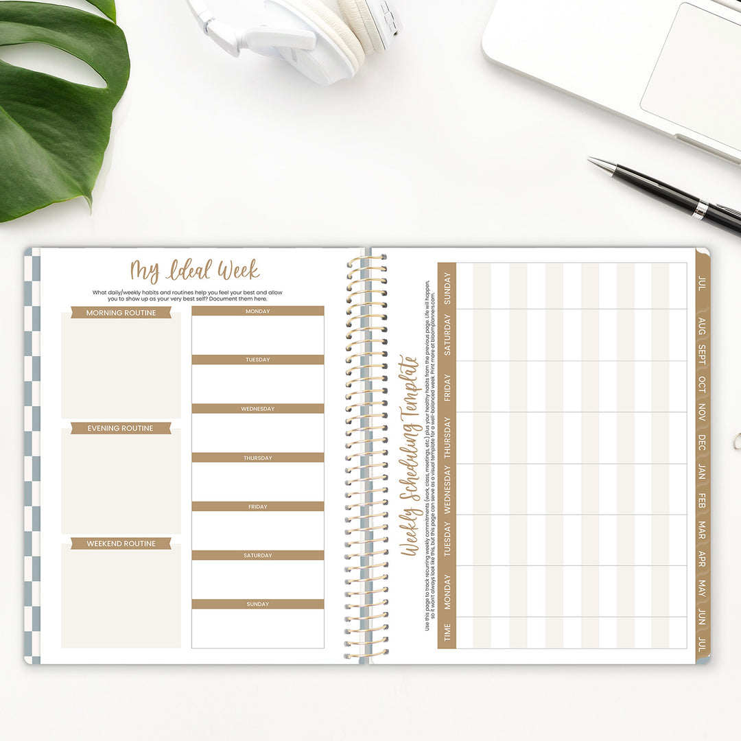 Weekly planner with a pen and plant on a white surface