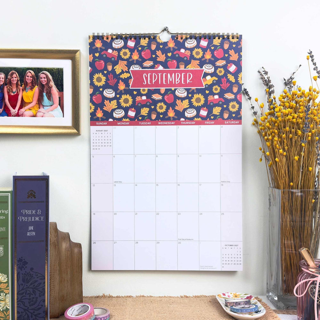 Wall calendar with floral design and September text, placed on a surface with books and decor items.