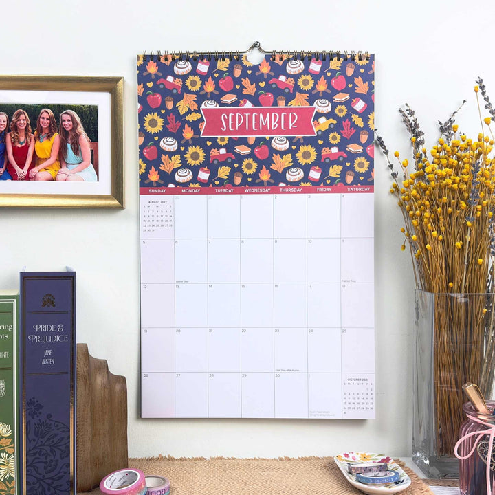 Wall calendar with floral design and September text, placed on a surface with books and decor items.
