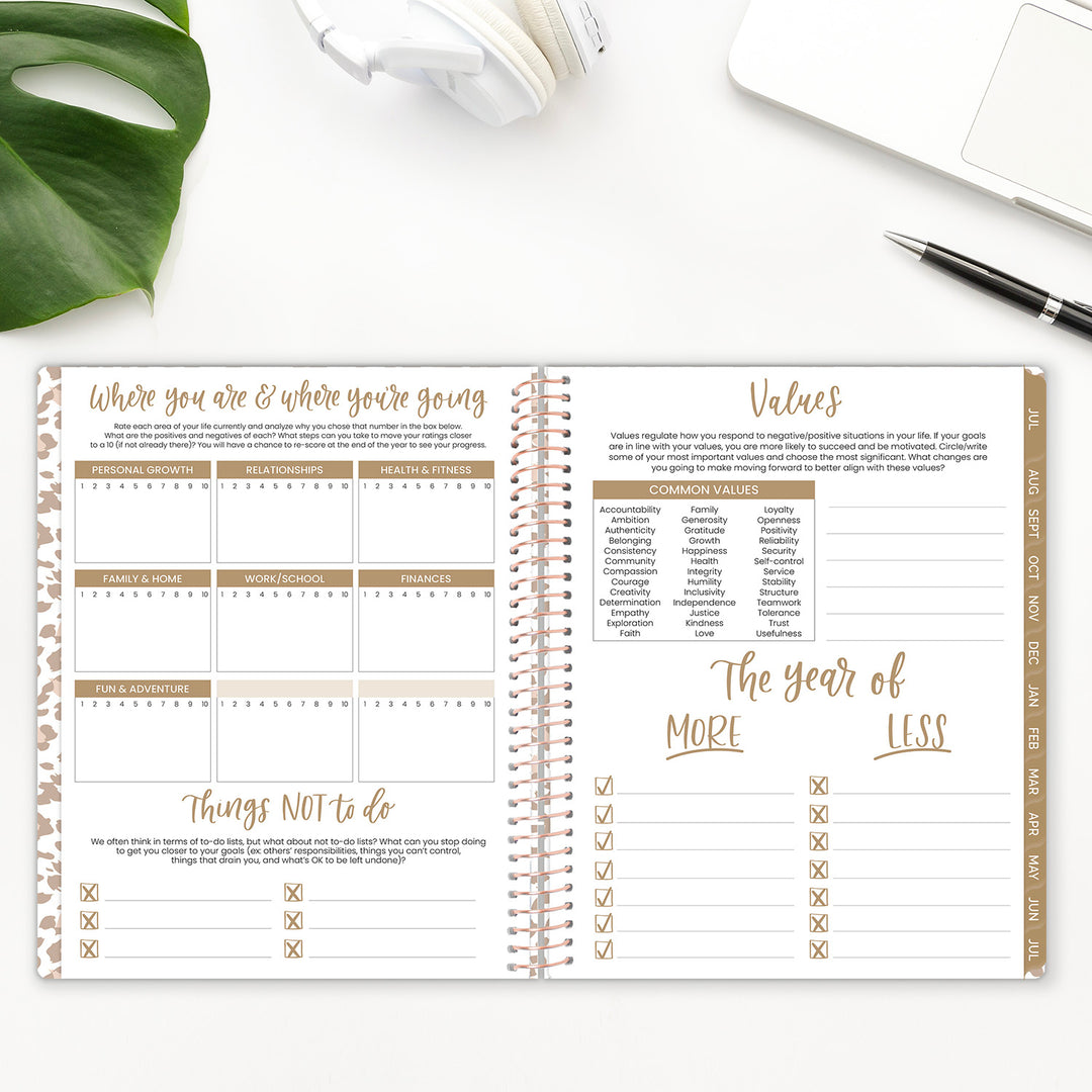 Open spiral-bound planner on a white surface with a pen and plant leaf visible