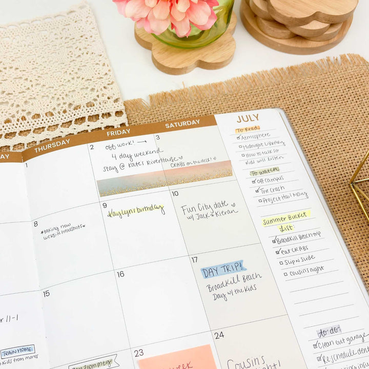 Calendar with July notes on a desk with flowers and wooden items