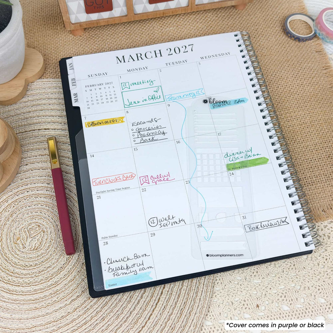 A spiral-bound planner or notebook showing a March 2027 calendar page, photographed on a woven beige surface with a pen nearby. The cover is partially visible and appears to be purple or black.