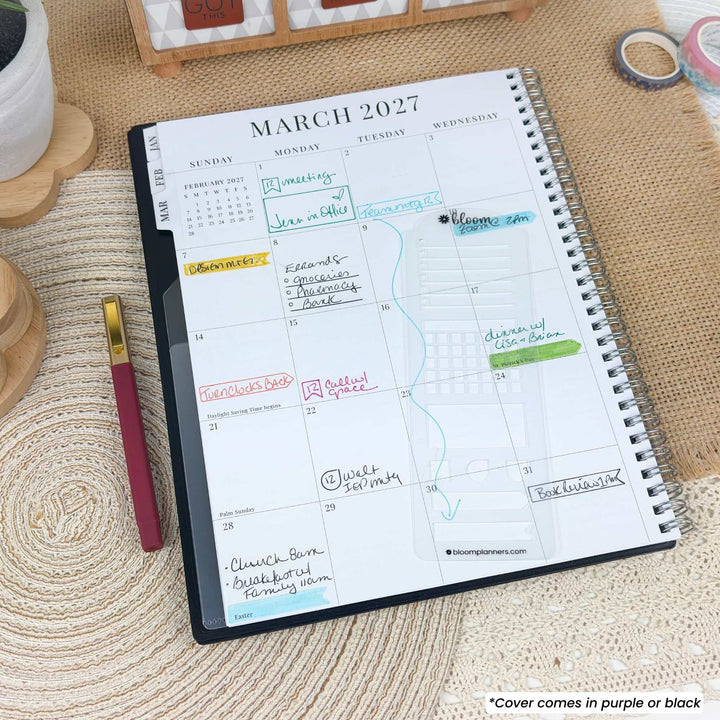 A spiral-bound planner or notebook showing a March 2027 calendar page, photographed on a woven beige surface with a pen nearby. The cover is partially visible and appears to be purple or black.