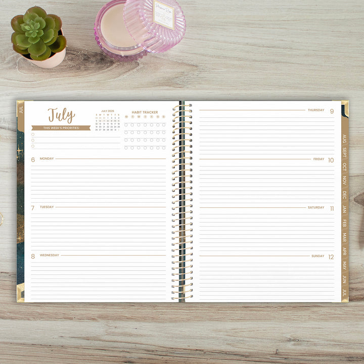 Open planner showing July on a wooden surface with a plant and candle.