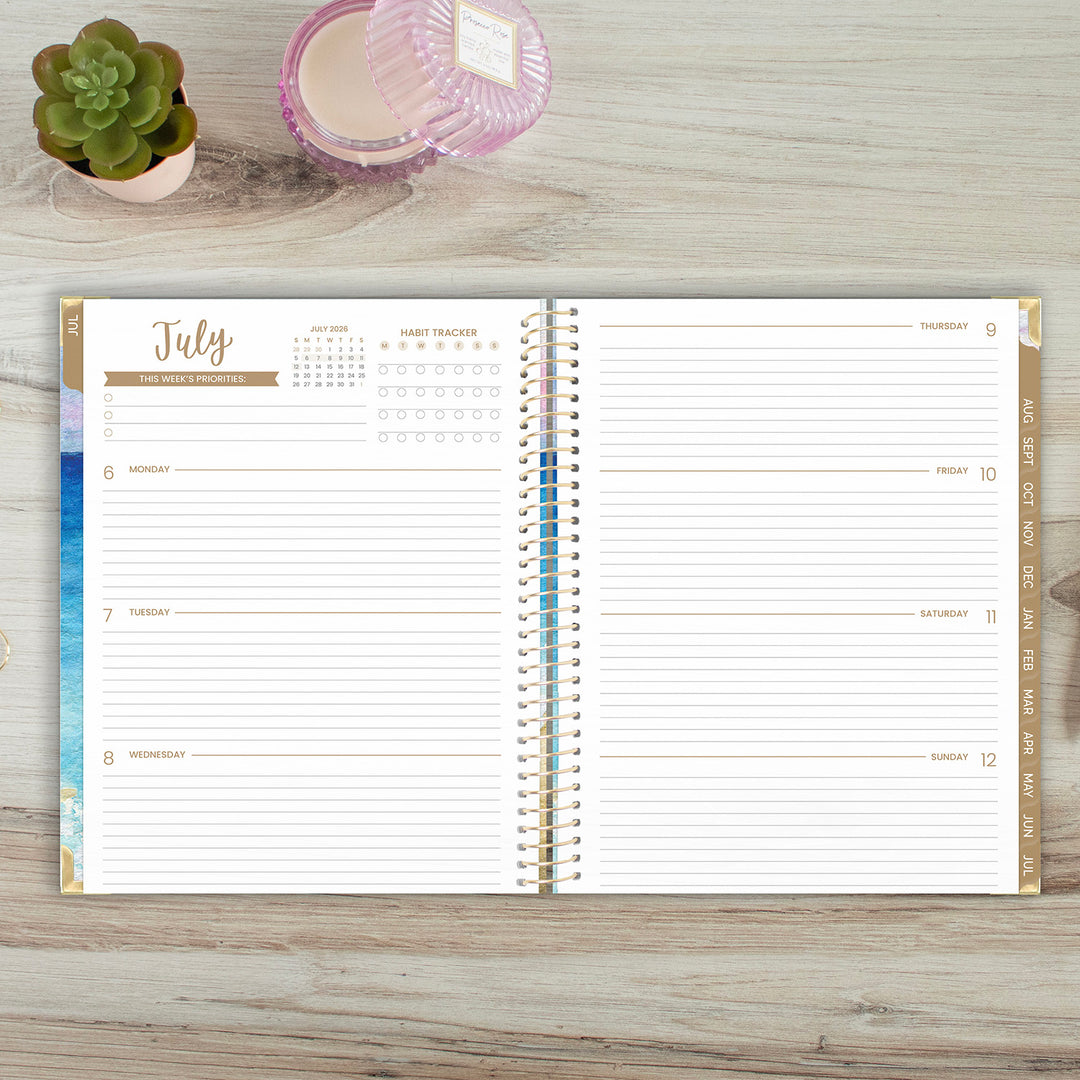 Open planner showing July monthly layout on a wooden surface with a small plant and container.