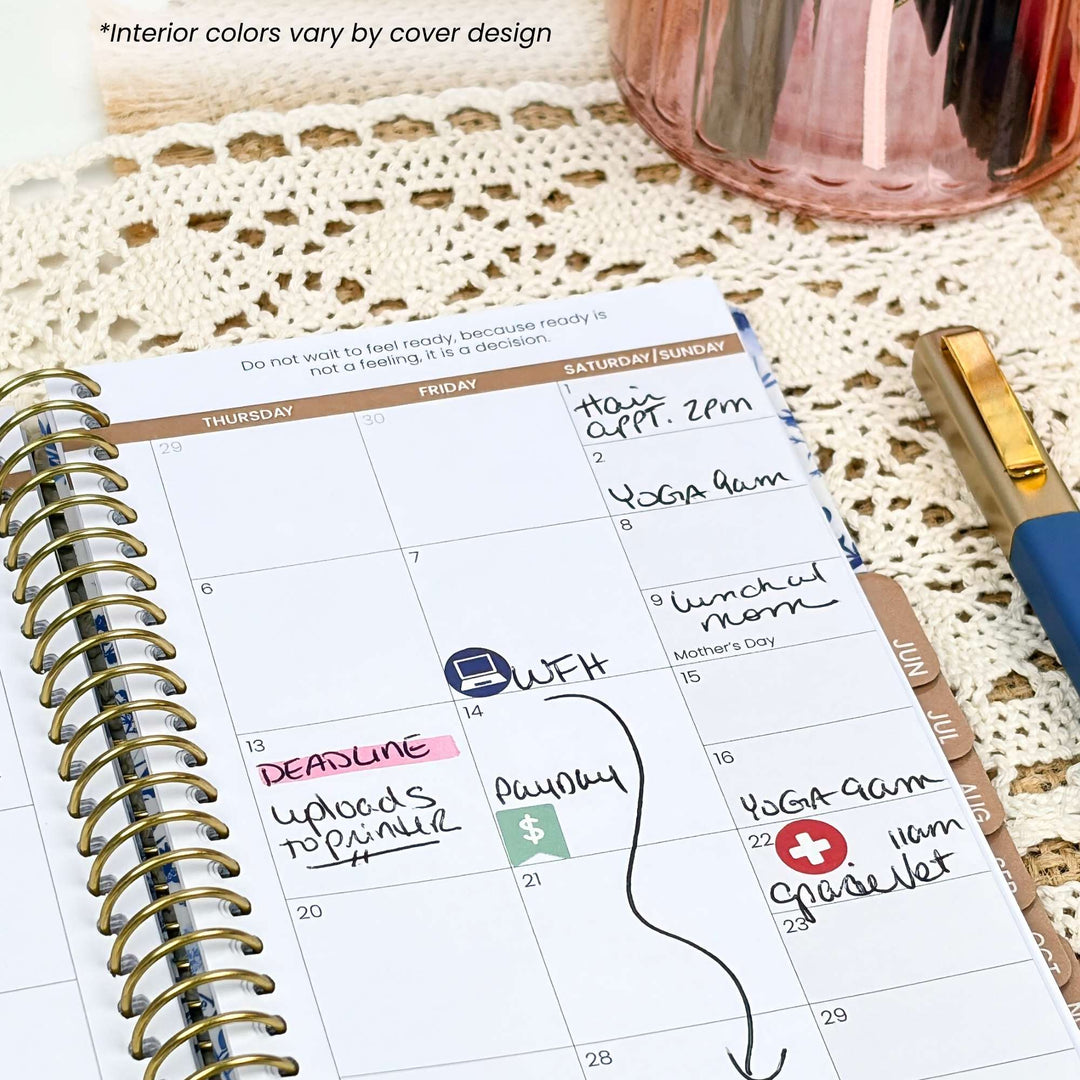 A spiral-bound planner page showing a weekly calendar layout with handwritten notes, placed on a cream lace surface with a pink cup and a blue-and-gold pen nearby.