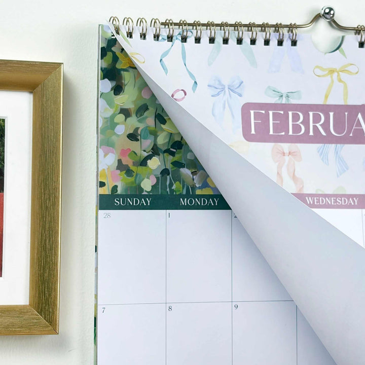 Calendar with a floral design on the left page and a white background on the right, with a wooden frame partially visible.