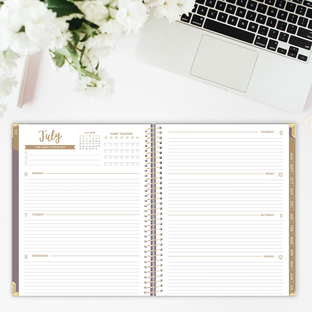 Open planner with July calendar on a desk with a laptop and flowers.