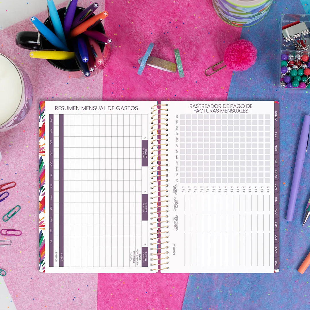 Spiral-bound planner with two different tracking pages on a colorful desk with stationery items.