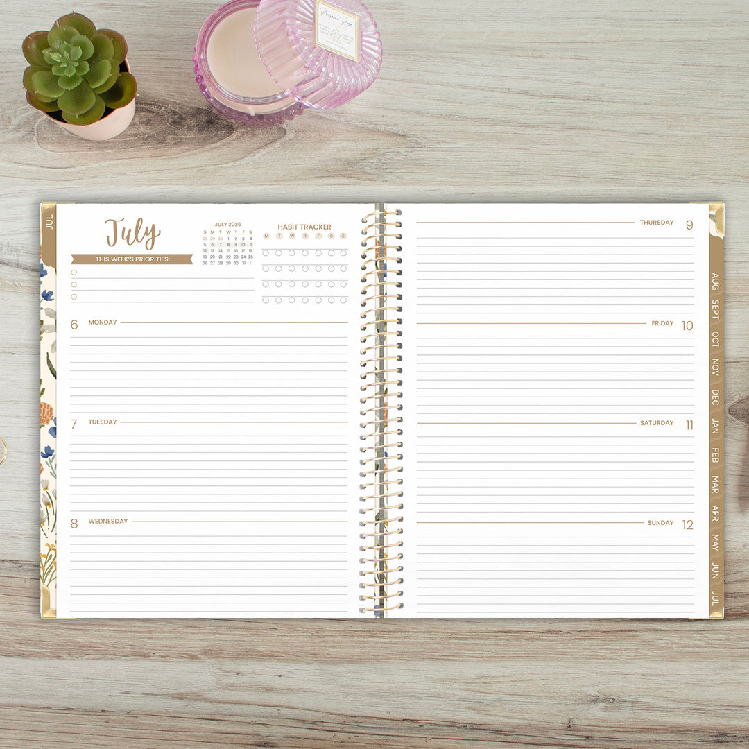 Open planner on a wooden surface with a small plant and container in the background