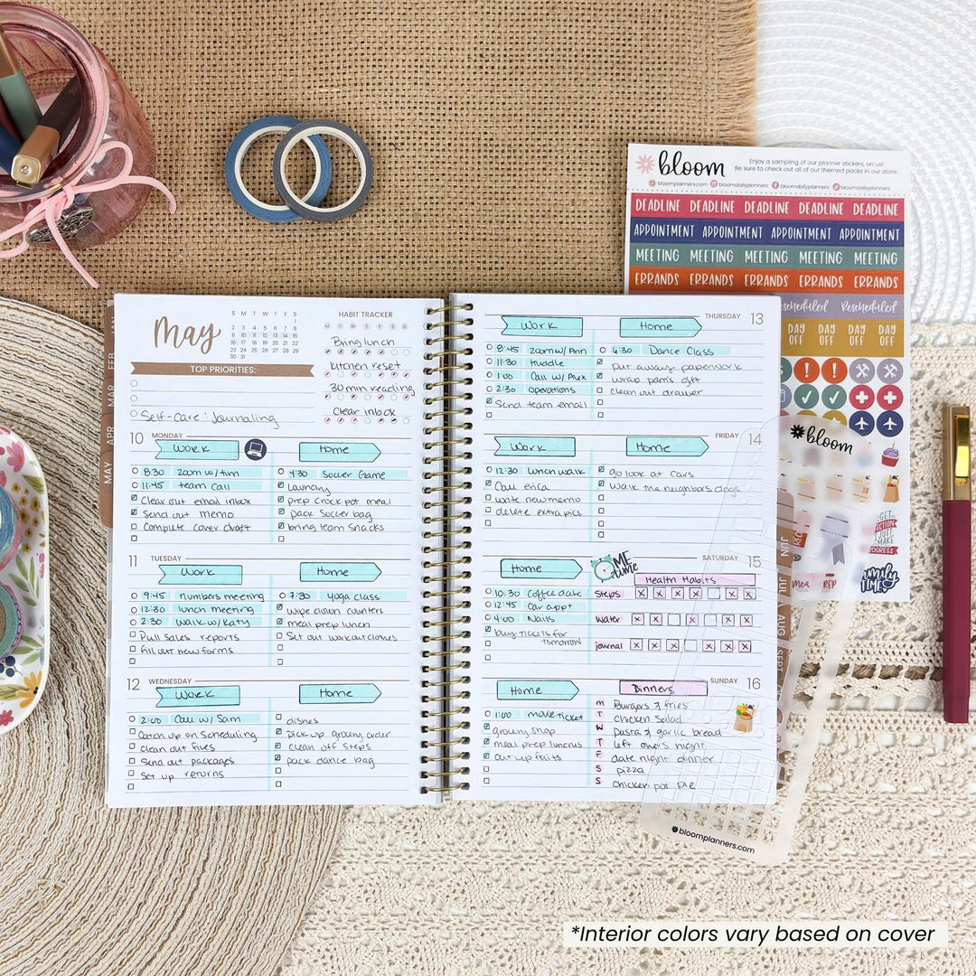 An open spiral-bound planner or journal spread on a woven beige surface, showing weekly planner pages with handwritten notes and colorful headers. Surrounding props include a pink pen, a small jar of pens, two blue rings, a sticker sheet labeled bloom, and a decorative item on the left.