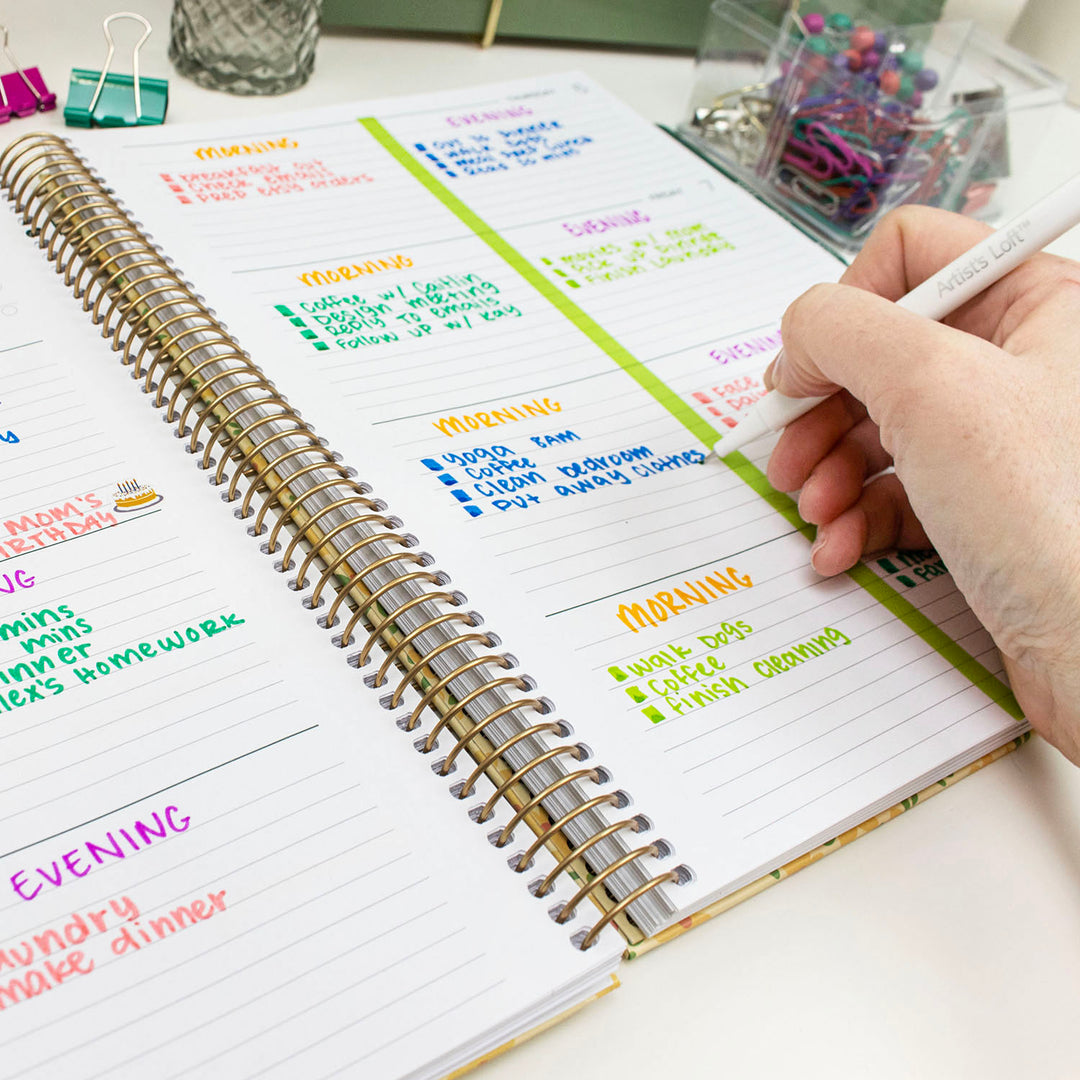 Person writing in a planner with colorful notes on a desk.