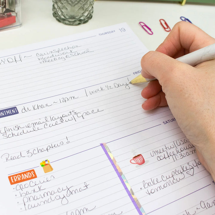 Hand writing in a planner with colorful paper clips on a desk