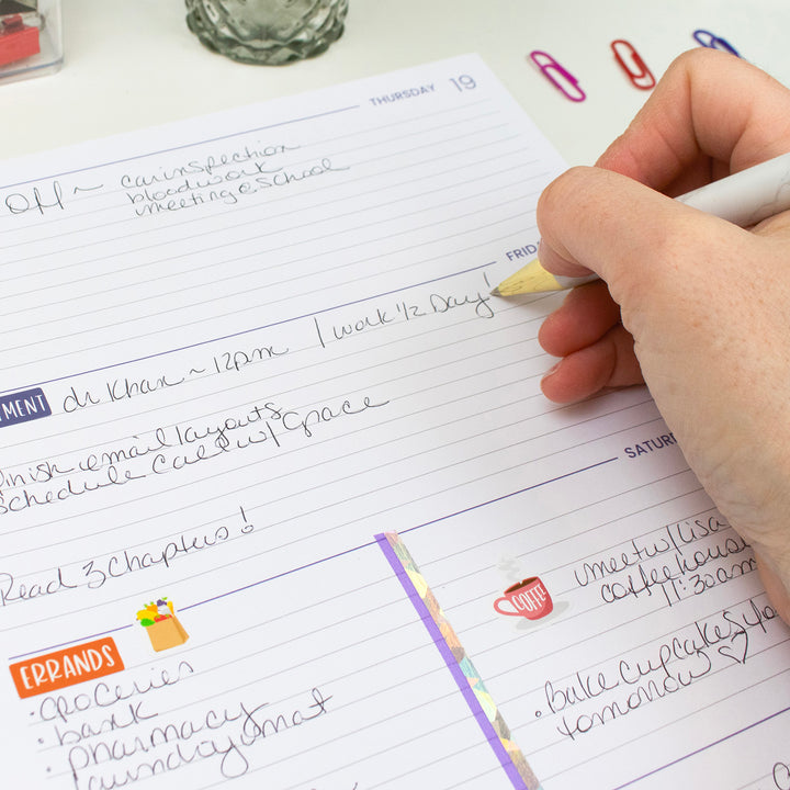 Hand writing in a planner with colorful paper clips on a desk