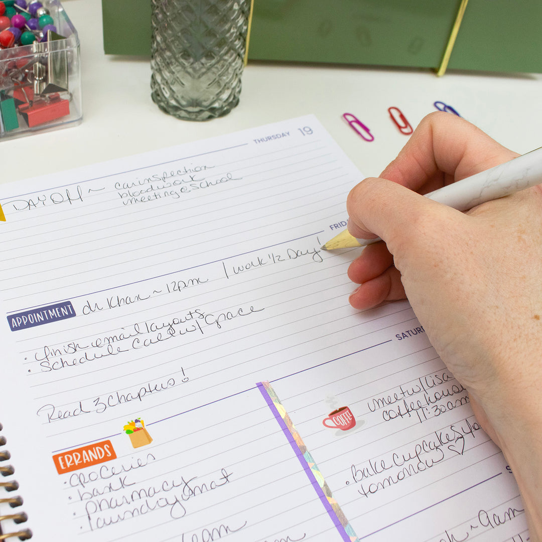 Person writing in a planner with colorful paper clips on a desk