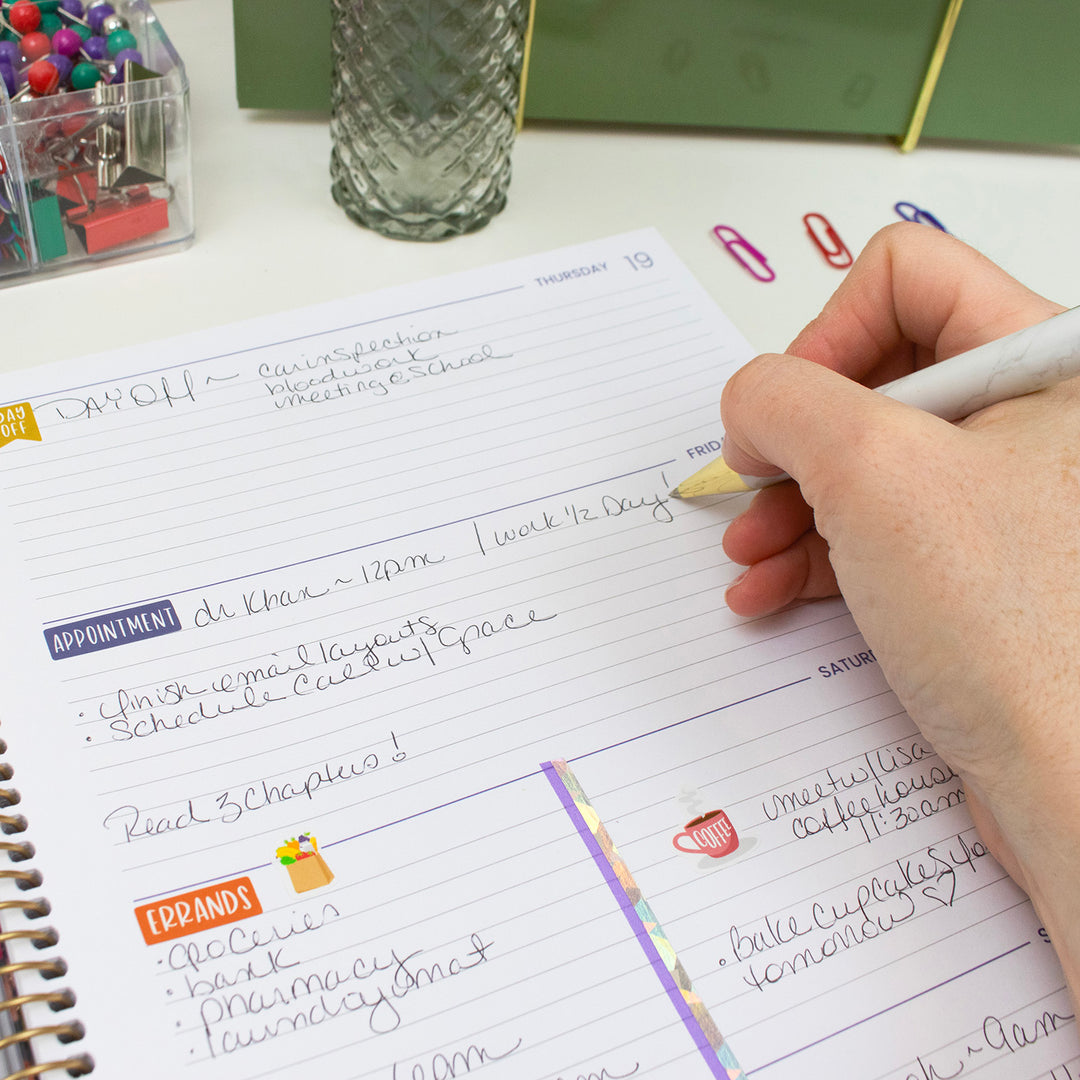 Person writing in a planner with colorful stickers on a desk.