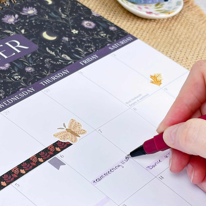 Person marking a date on a floral-patterned calendar with a pen.