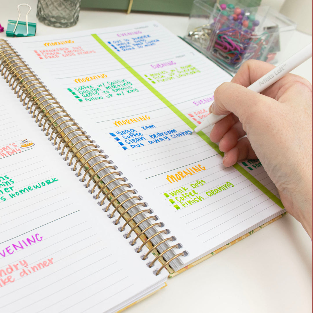 Person writing in a planner with colorful notes on a desk.