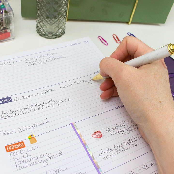 Hand writing in a planner with a pen on a desk.