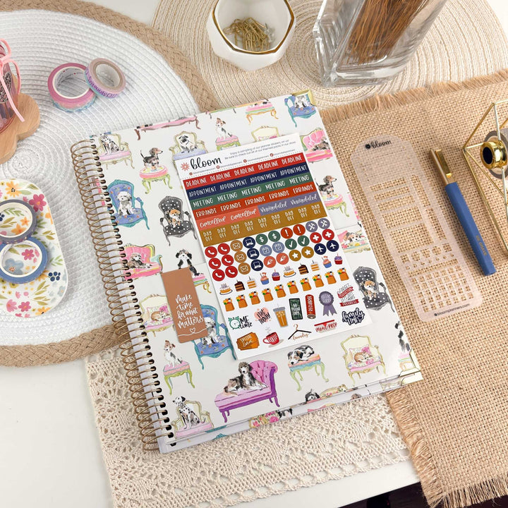 A spiral-bound planner or notebook with colorful illustrated stickers and a planner insert sheet, styled on a tabletop with pens, washi tape, a cup, and other stationery props.