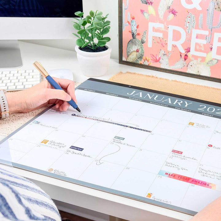 A hand writing on a January 2027 desk calendar on a desk. 