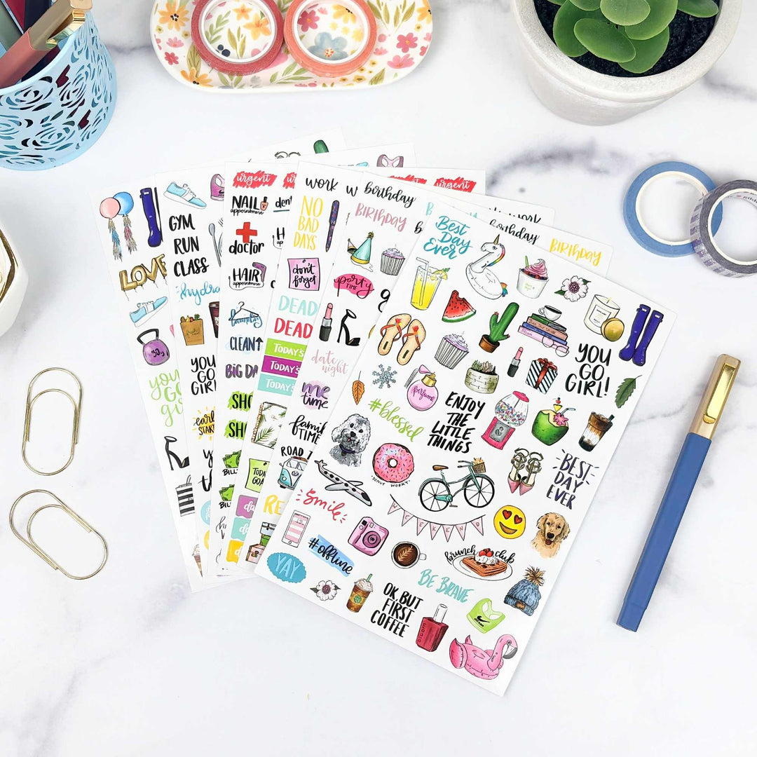 Sheet of colorful planner stickers on a white surface with stationery items.