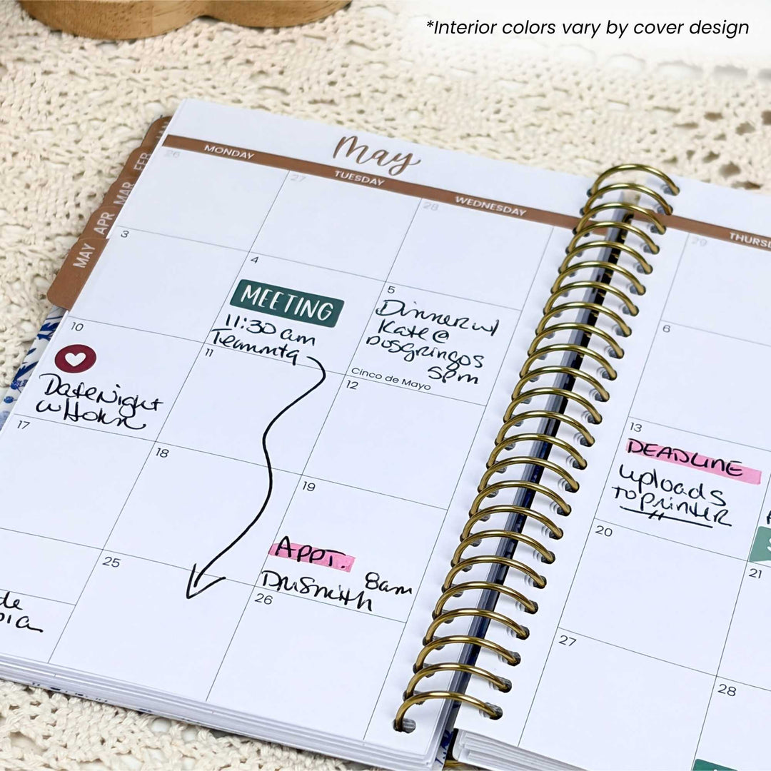Open planner with May calendar page showing appointments and notes on a textured surface.