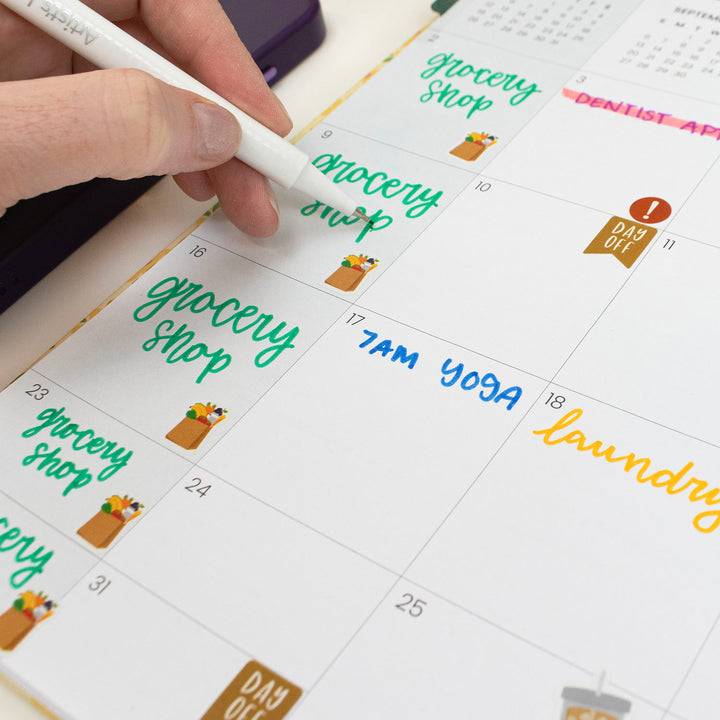 Hand writing on a calendar with colorful text and icons