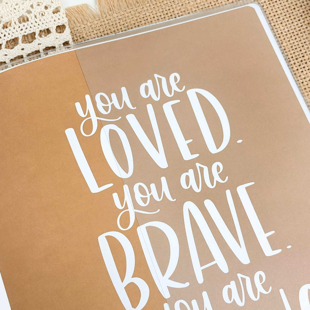 Motivational quote card with 'you are loved, you are brave' text on a brown background
