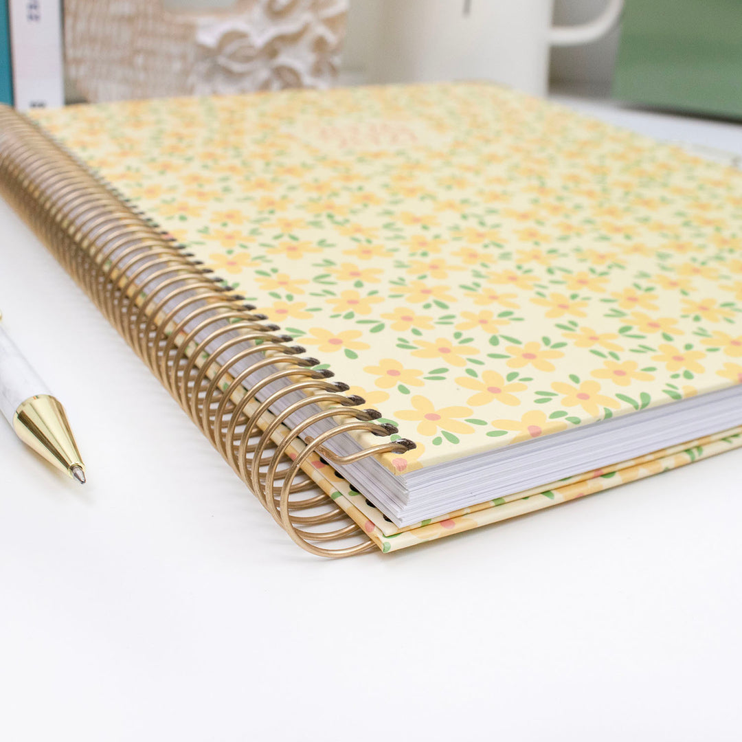 Planner with floral cover and gold spiral binding on a white surface