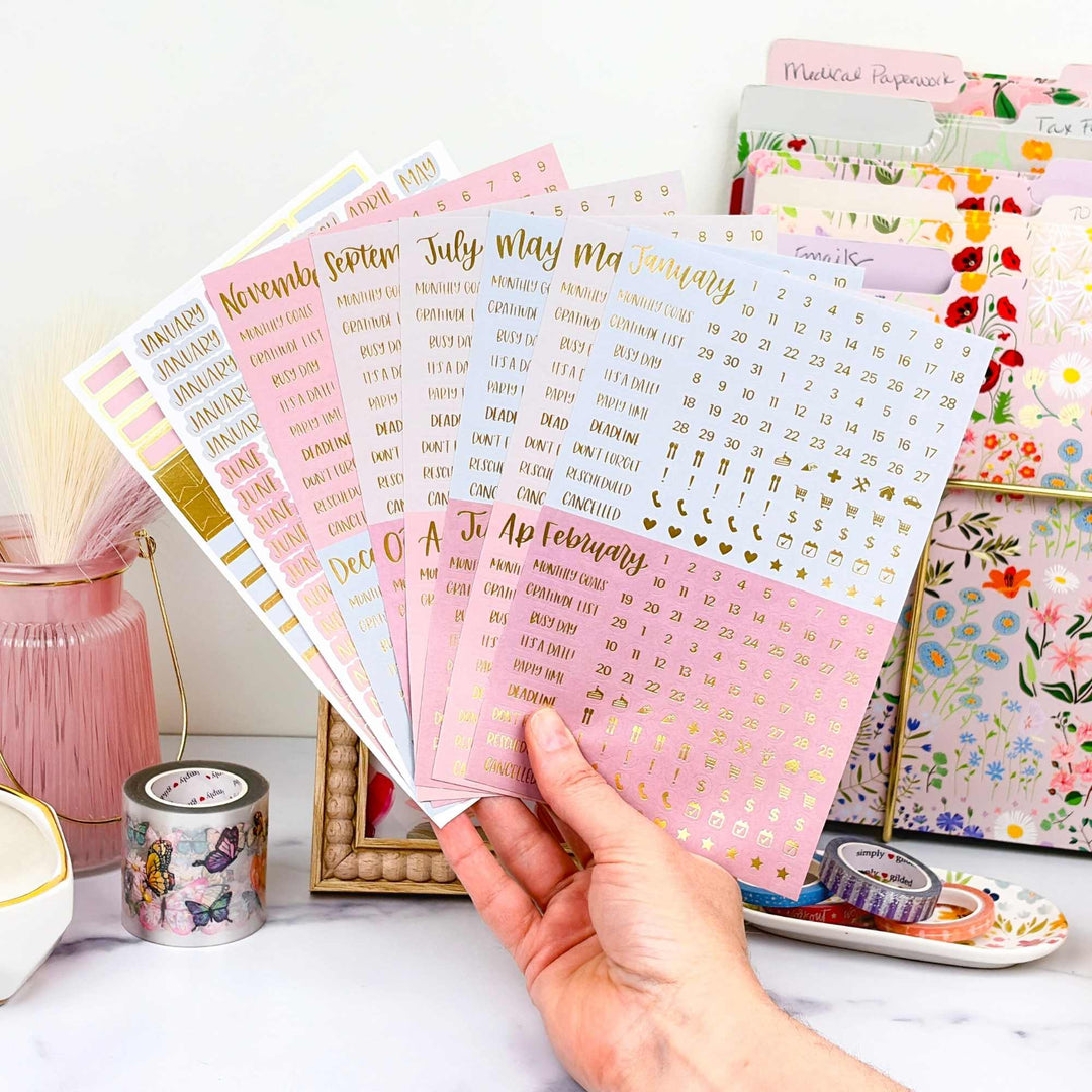 Hand holding a stack of decorative calendar essential planner stickers in matte jewel tone colors.