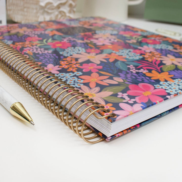 Floral planner with gold spiral binding on a white surface