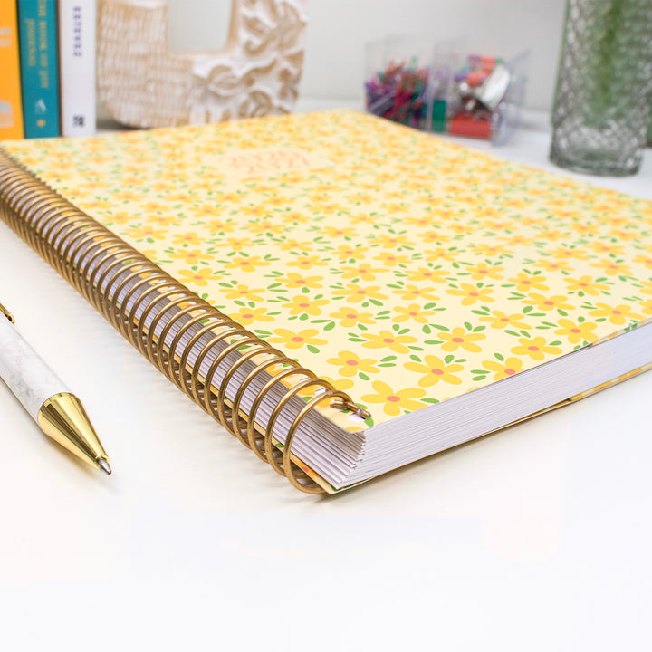 Planner with floral cover and gold spiral binding on a white surface