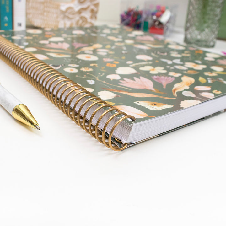 Floral planner with gold spiral binding on a white surface
