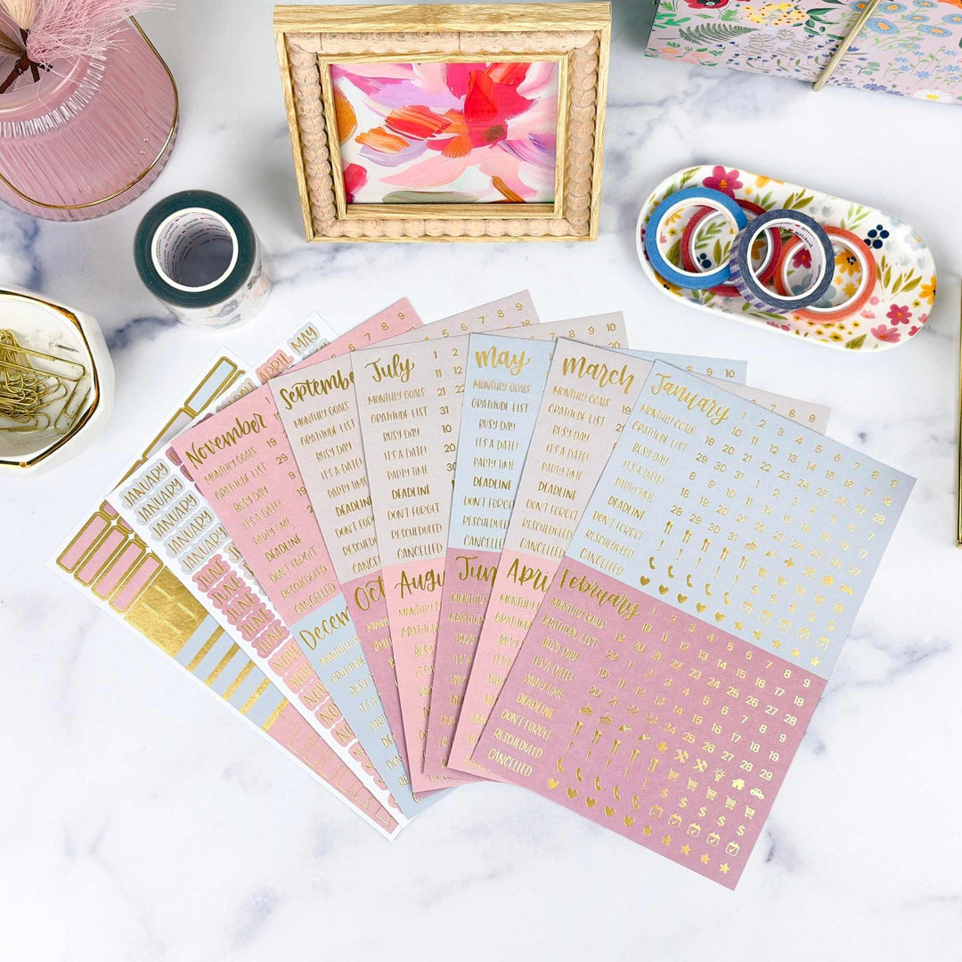 Set of planner stickers with gold text on a marble surface with stationery items.