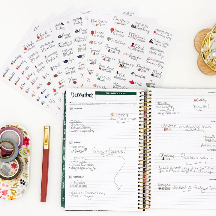 Open planner with holiday celebration sticker sheets and handwritten notes, gold spiral