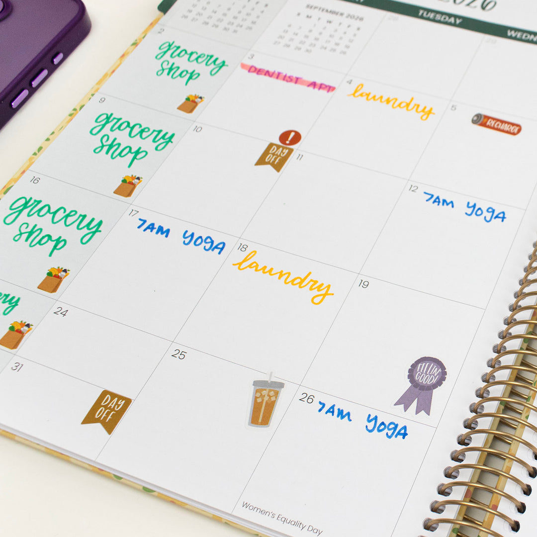 Calendar with stickers labeled 'grocery shop', '7am yoga', and 'laundry' on a white surface.