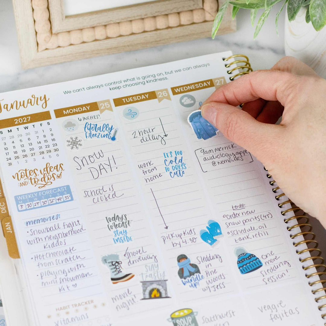 Planner with stickers and a hand interacting with it on a light surface.
